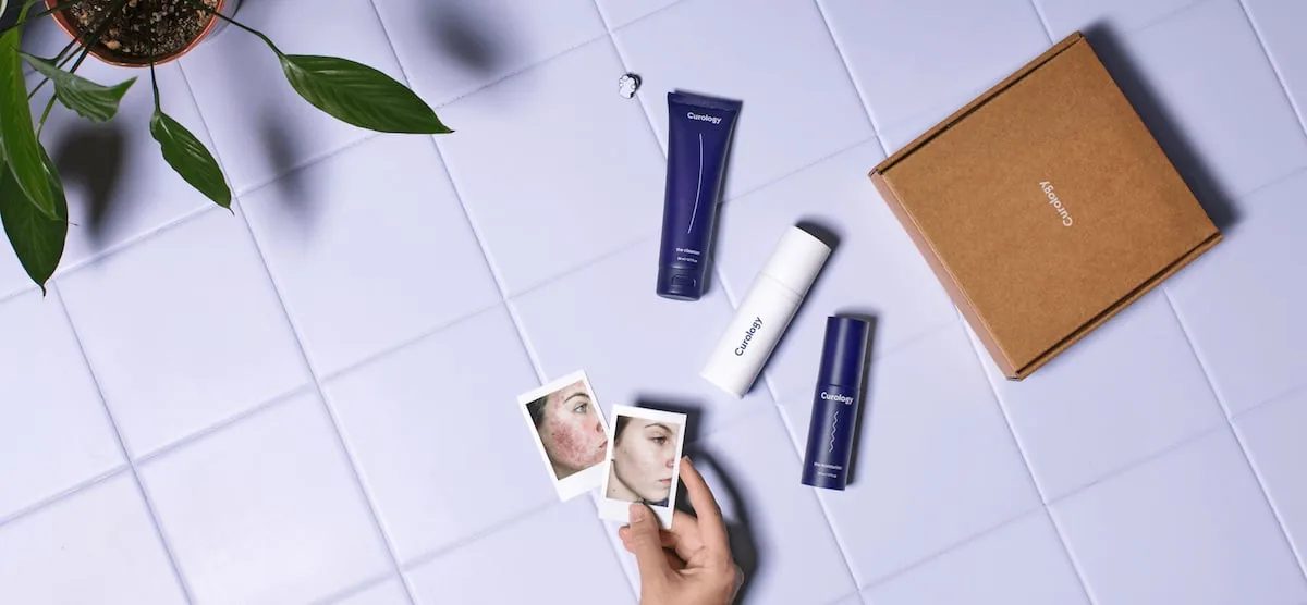 Curology's own photo of its dark blue prescription bottles, a white tube and a brown shipping box on light purple tiles.